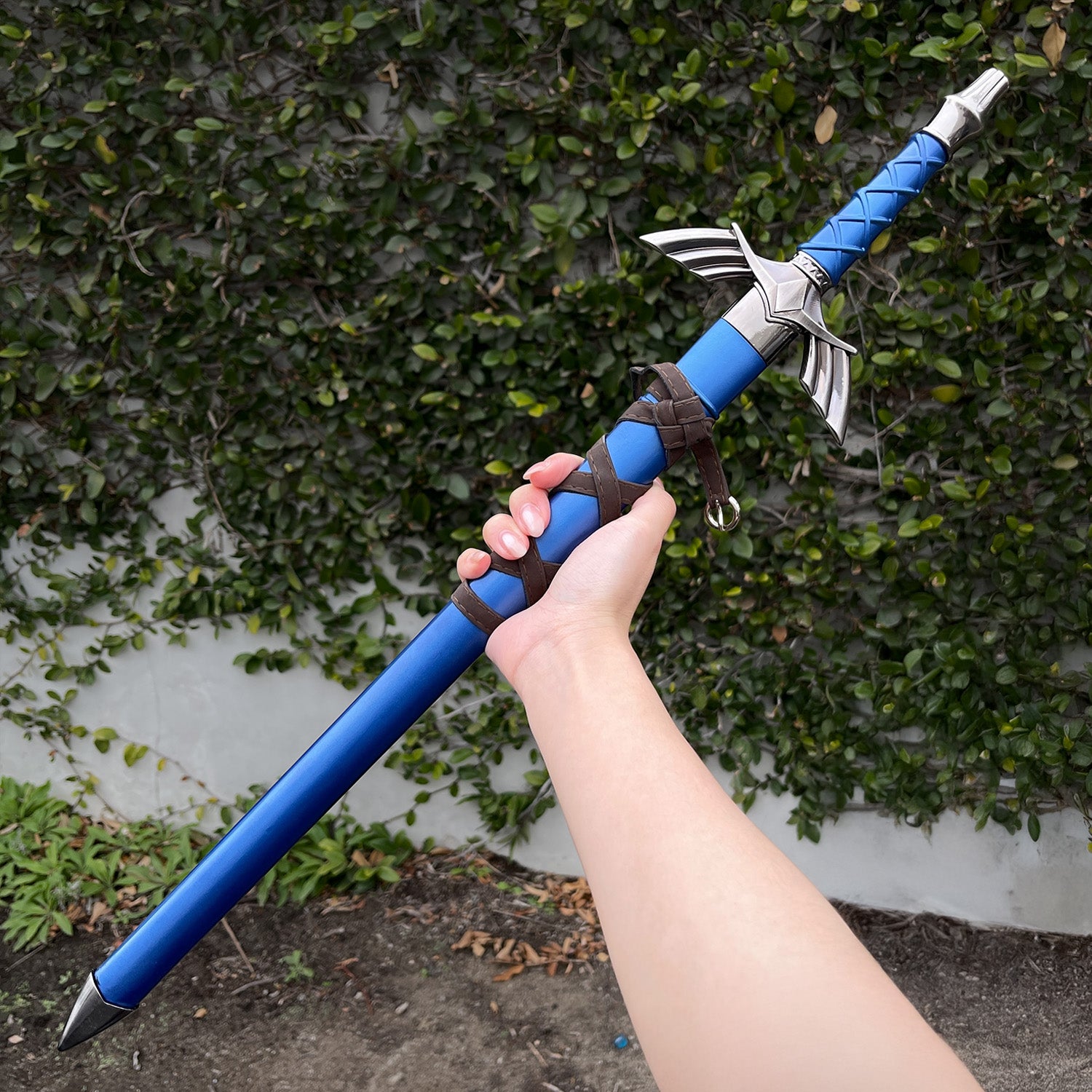 Hand holding blue fantasy sword outdoors