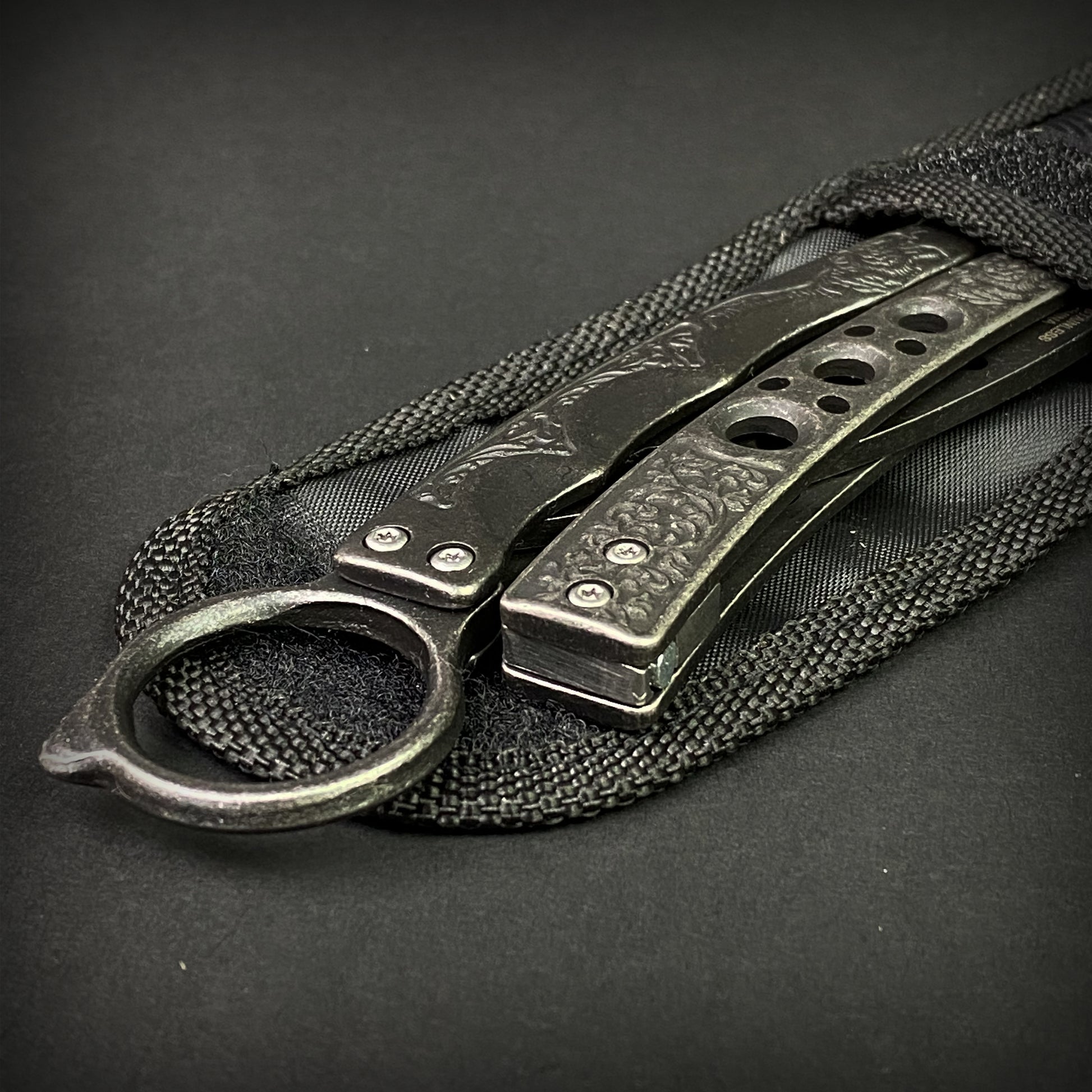 Guild Arms black butterfly trainer knife with textured metal handles resting on a black sheath