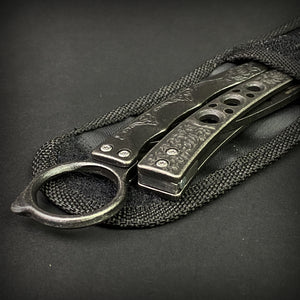 Guild Arms black butterfly trainer knife with textured metal handles resting on a black sheath