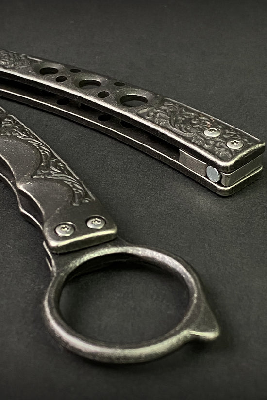 Guild Arms black butterfly trainer knife with detailed engraved metal handles on dark background