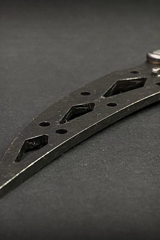 Close-up of Guild Arms black butterfly trainer knife blade with cut-out designs on black background