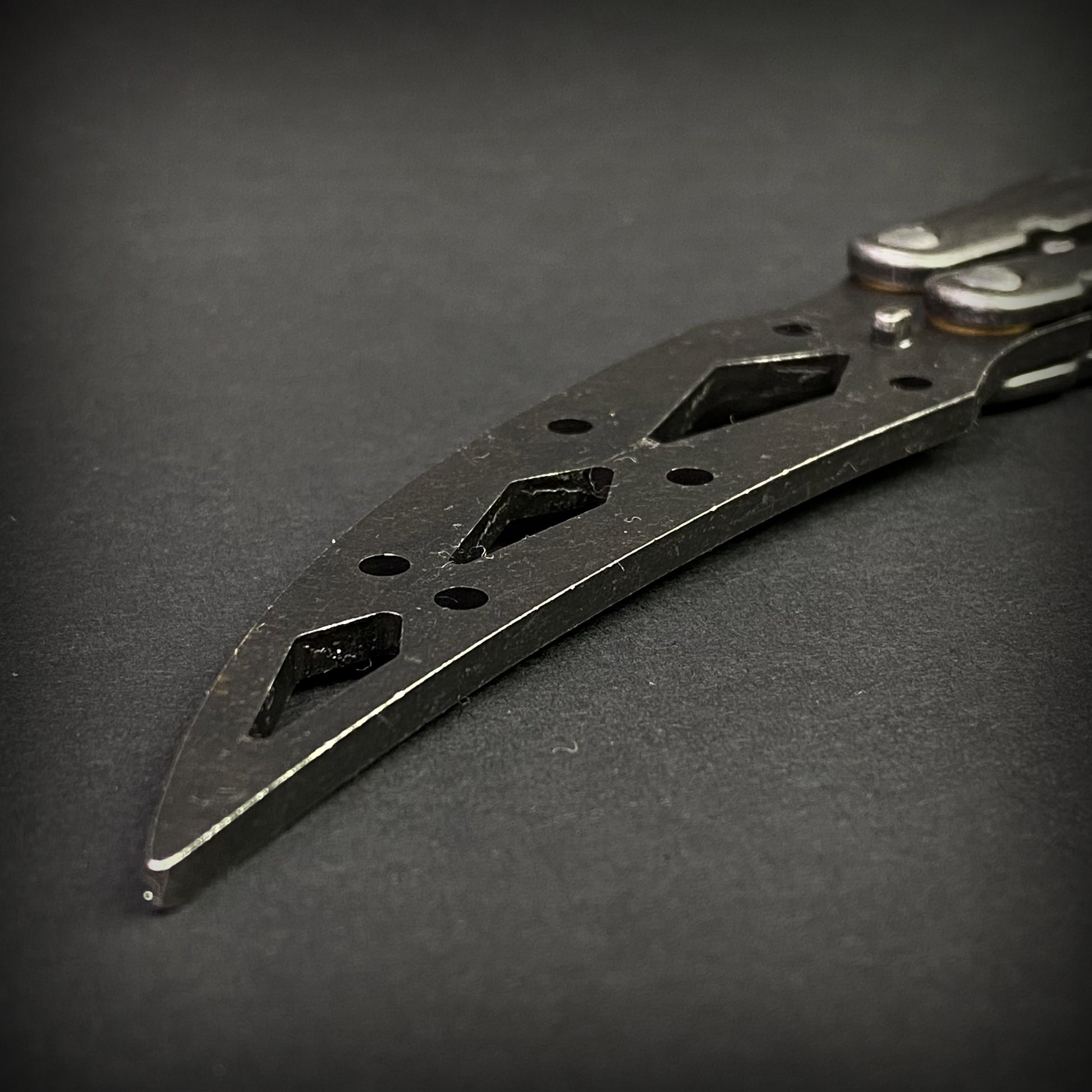Close-up of Guild Arms black butterfly trainer knife blade with cut-out designs on black background