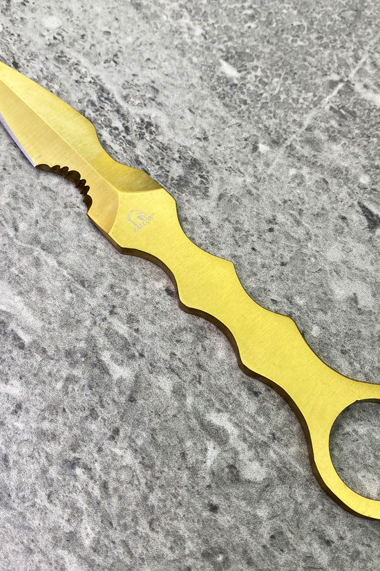 falcon tactical knife fixed blade gold anodized ring handle with ergonomic finger grooves on gray stone background