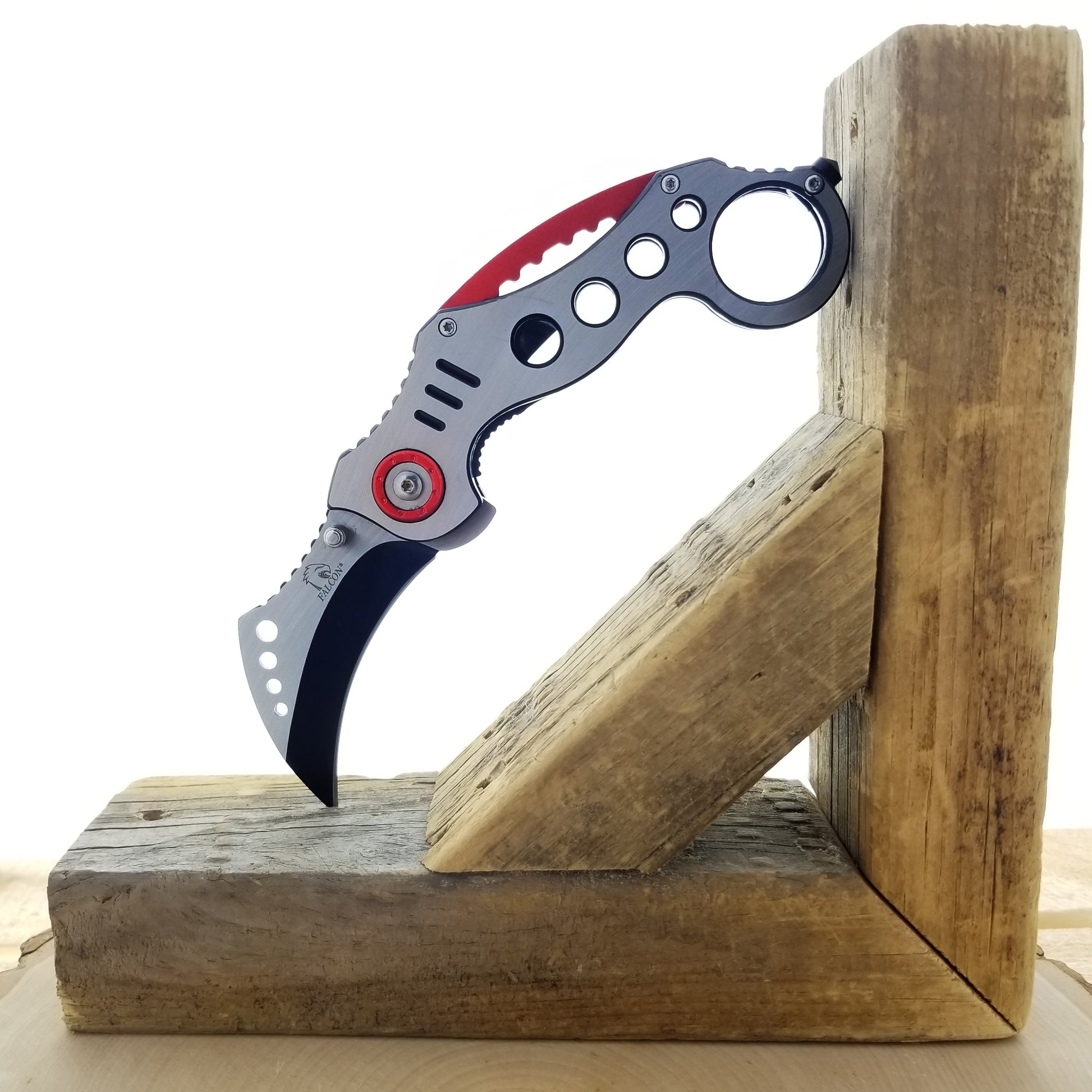 Falcon Red Karambit Spring Assisted Knife displayed on a wooden block for ergonomic design showcase