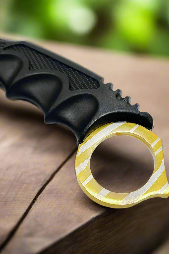 Close-up of Falcon trainer karambit knife handle with textured grip and gold ring on wooden surface