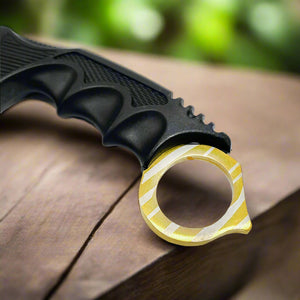 Close-up of Falcon trainer karambit knife handle with textured grip and gold ring on wooden surface