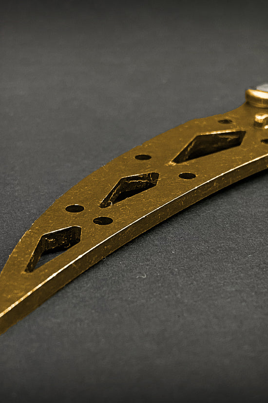 Close-up of gold butterfly trainer knife blade with cutout design by Guild Arms on dark background