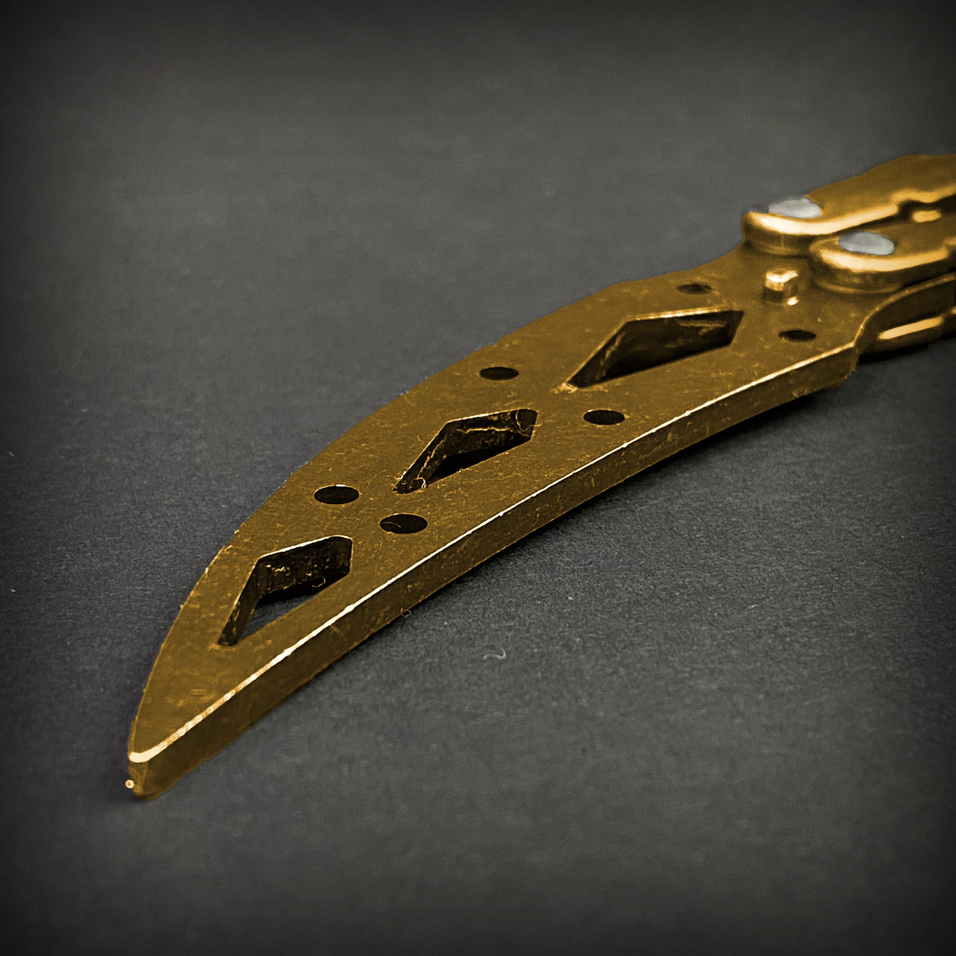 Close-up of gold butterfly trainer knife blade with cutout design by Guild Arms on dark background