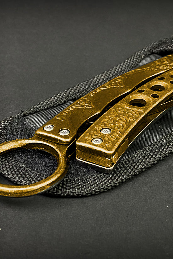 Guild Arms gold butterfly trainer knife with detailed textured handles on black fabric sheath
