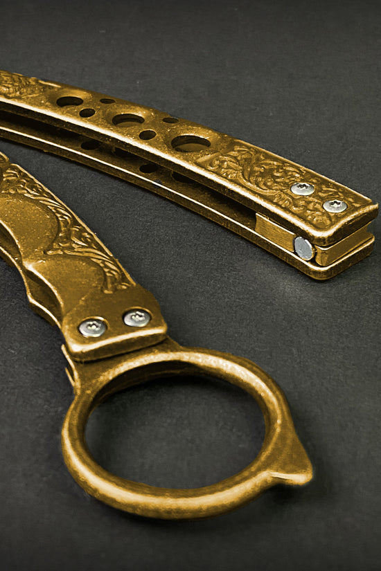 Guild Arms gold butterfly trainer knife with decorative handle and hole-pattern design on black background