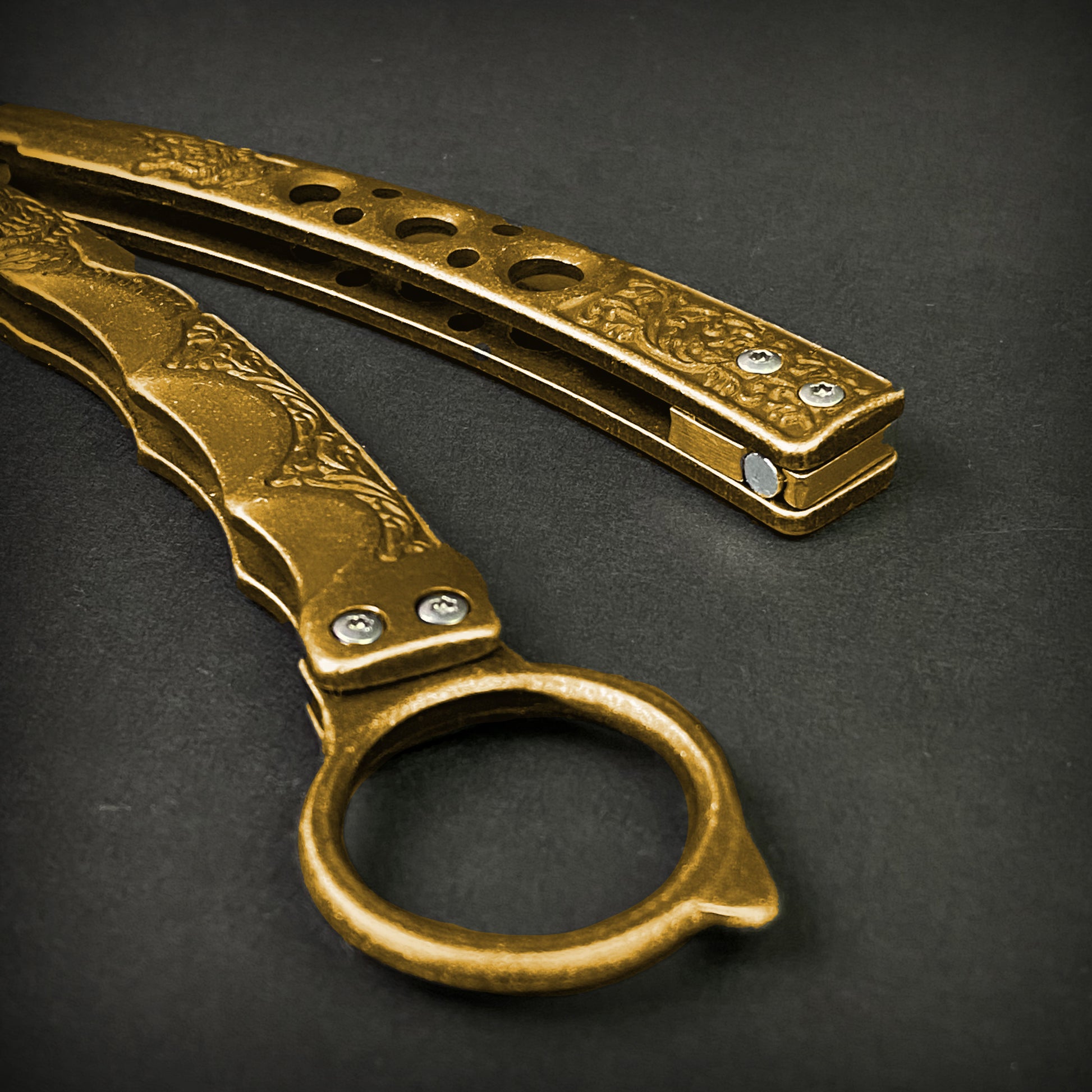 Guild Arms gold butterfly trainer knife with decorative handle and hole-pattern design on black background