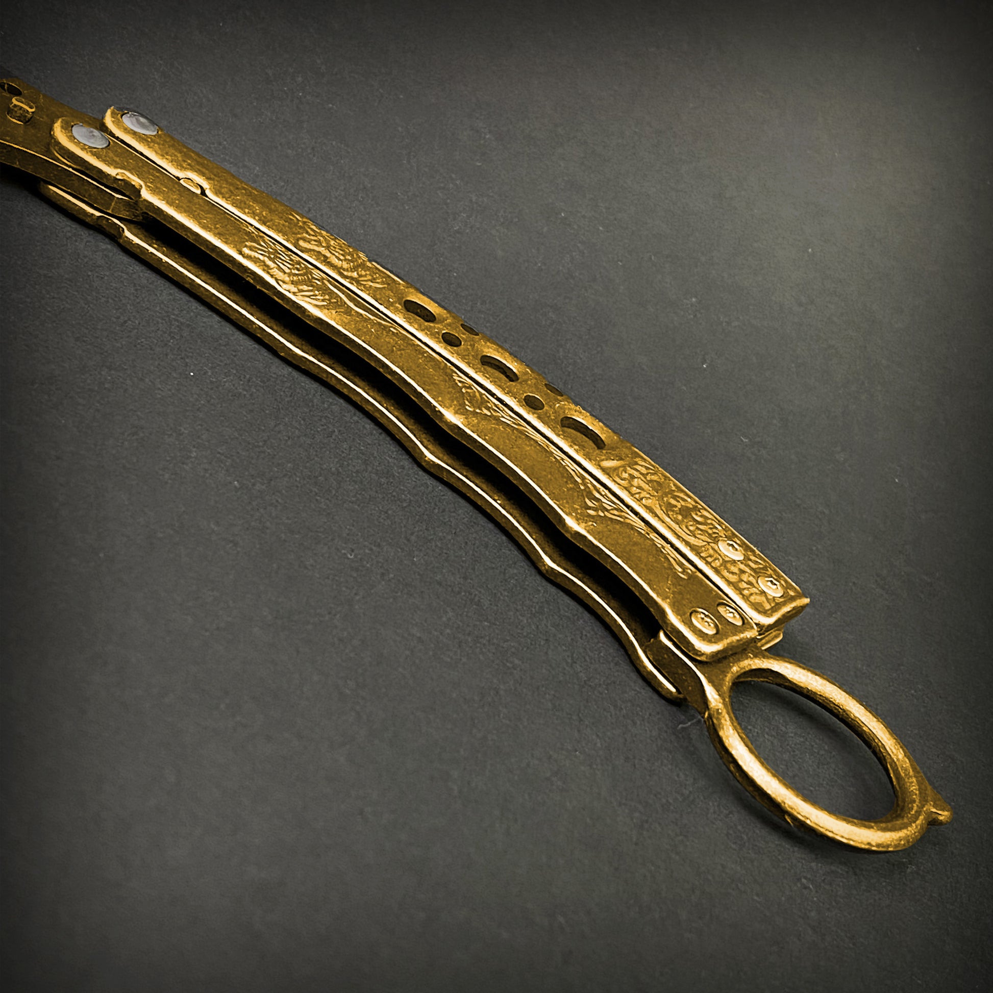 Guild Arms gold butterfly trainer knife with engraved handles on a dark surface