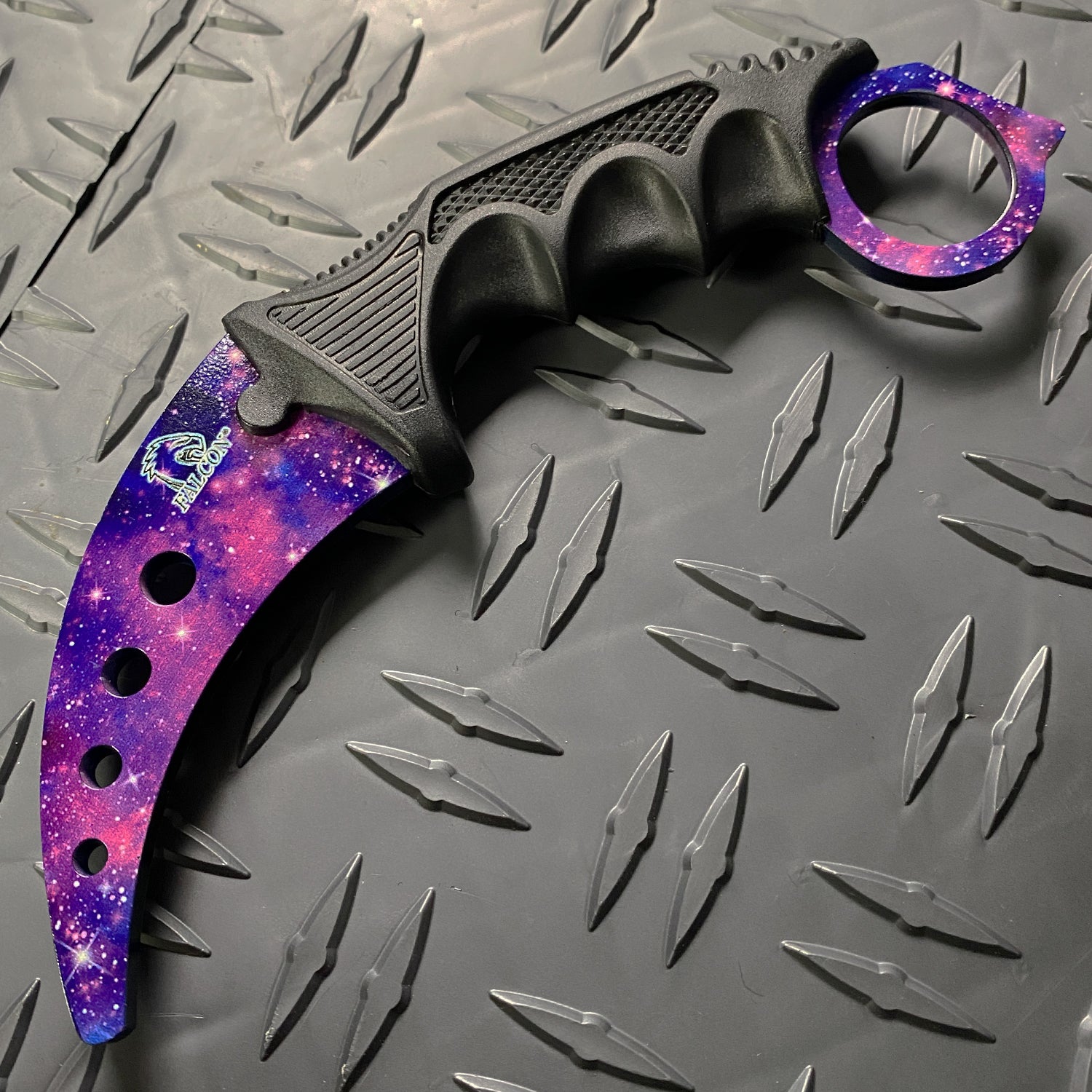 Falcon purple karambit trainer knife with galaxy design and ergonomic black handle on textured metal surface