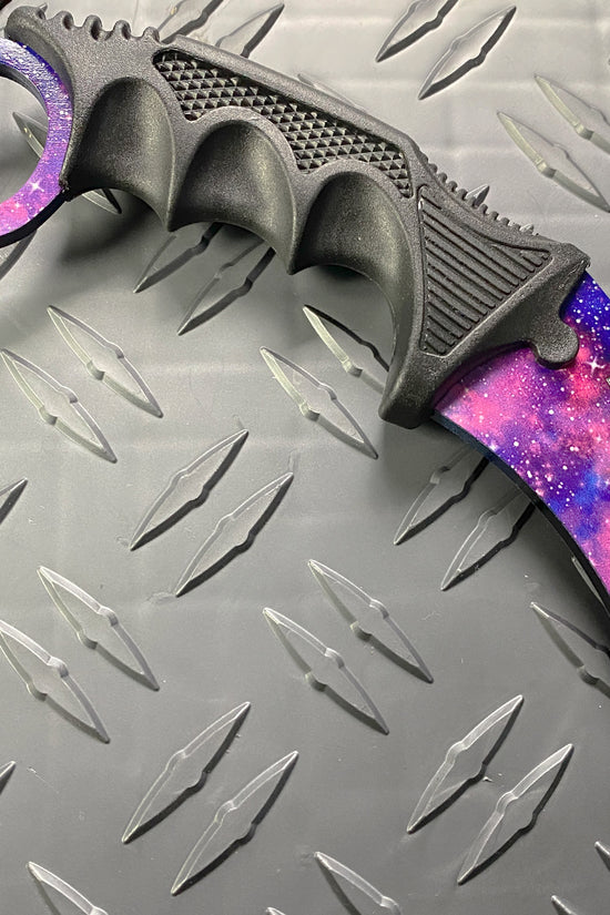 Falcon purple karambit trainer knife with galaxy design and textured black grip on metal background